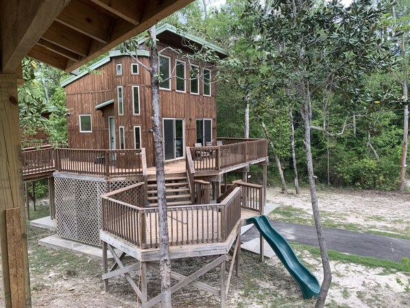 A multi-level wooden cabin with a deck and a slide, surrounded by trees.