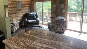 A cozy room with a wooden interior, a marble table, two patterned chairs, a massage chair, and a large sliding glass door leading to an outdoor deck. - Cozy Cabin on the River (D'Iberville)
