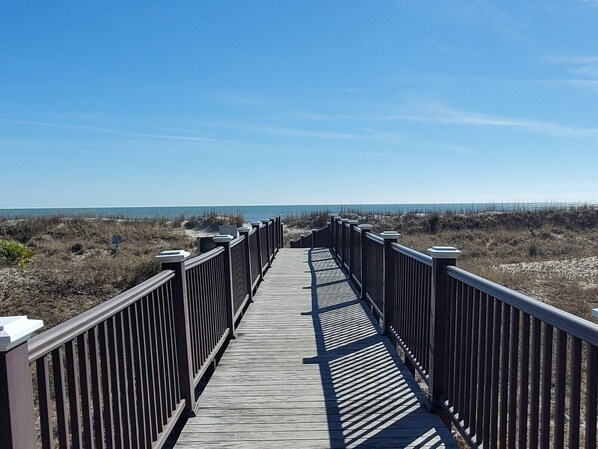 A wooden boardwalk leading to a beach with a clear sky.