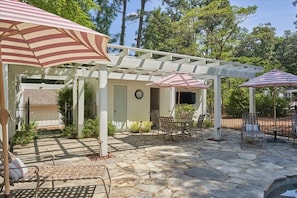 A covered patio area with stone flooring, outdoor furniture, and striped umbrellas.