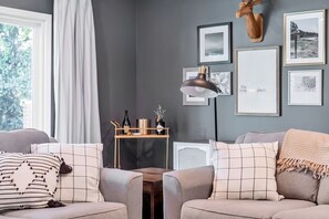 A cozy living room with a grey sofa, a wooden coffee table, and a mounted deer head. There are framed pictures on the wall and a lamp on a side table.