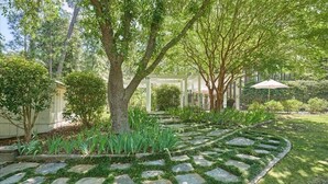 Un jardin avec un chemin de pierre, des arbres et une pergola.