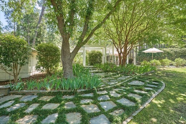 A garden with a stone pathway, trees, and a pergola.