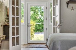 A room with a door leading to a garden, a bed with a white bedspread, and a small table with a vase. - Spacious:  swimming pool, walk to the village. (Pinehurst)