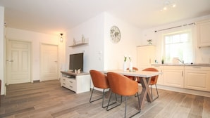A modern kitchen with white cabinets, a dining table with orange chairs, and a clock on the wall.
