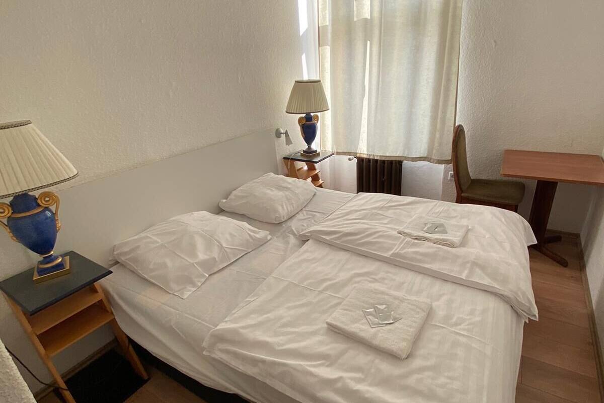 A neatly made bed with white linens, a bedside lamp, and a small table with a lamp.