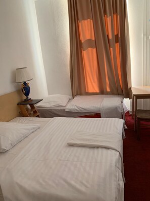 Una habitación de hotel con dos camas, una mesita de noche con lámpara y una ventana con cortinas.