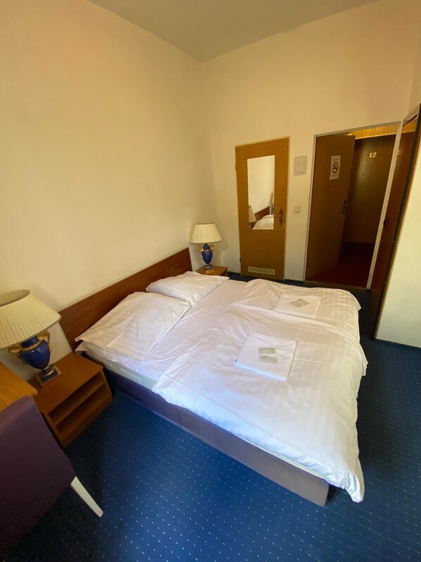 A hotel room with a large bed, a nightstand with a lamp, a mirror, and a door to another room. - Märkischer Hof (Berlin)