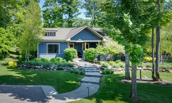 A two-story house with a front porch, stone retaining wall, and a well-maintained lawn. - Private 4 Bedroom-8 Bed Cottage Near Ski Resorts! Stay at True North Golf Club (Harbor Springs)