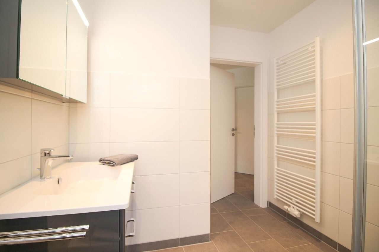 Un baño con lavamanos blanco, una toalla, un espejo y un radiador blanco.