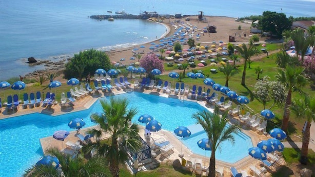 Un resort con una gran piscina rodeada de tumbonas y sombrillas, una zona de playa y vistas al mar.