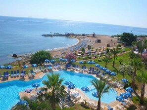 Un complexe hôtelier doté d’une grande piscine entourée de transats et de parasols, d’une plage et offrant une vue sur la mer.