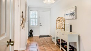 Un couloir avec une porte blanche, une console blanche dotée de tiroirs, une décoration murale et un panier posé sur le sol.