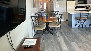 A modern kitchen with a central island, a dining area with a round table and chairs, and a flat-screen TV mounted on the wall. - 9A, Resting Beach Face (Destin)
