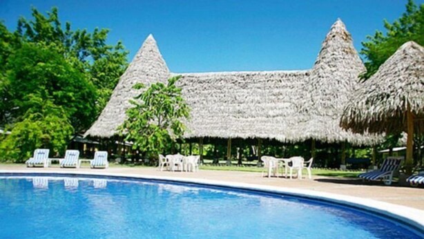 A swimming pool with lounge chairs and thatched-roof structures. - Rancho Casa Grande (Quepos)