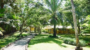 A garden with a gravel path, palm trees, and a yellow building. - Rancho Casa Grande (Quepos)