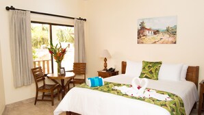 A hotel room with a bed, a dining table with chairs, a vase with flowers, and a painting on the wall. - Rancho Casa Grande (Quepos)