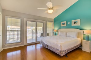 A bedroom with a large bed, a ceiling fan, and a view through the sliding glass doors.