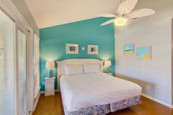 A bedroom with a large bed, two bedside tables with lamps, a ceiling fan, and artwork on the walls. - 3C, Vitamin Sea (Destin)