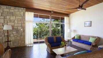 A spacious living area with wicker furniture, a stone wall, and large windows offering a view of greenery.