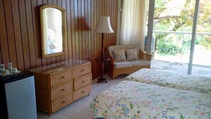 A room with a wooden dresser, a mirror, a lamp, a sofa, and two beds with floral bedding. - Frenchmans Cove (Port Antonio)