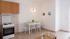 A compact kitchen with white cabinets, a stove, and a dining area with a table and chairs. - Marina Blue Studios (Mykonos)