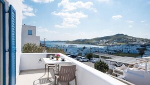 A balcony with a table and chairs, overlooking a coastal town with white buildings and a view of the sea. - Marina Blue Studios (Mykonos)