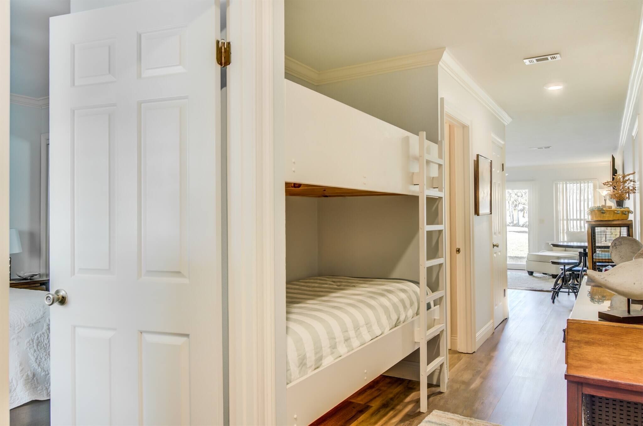 A bunk bed with a ladder, a white door, and a hallway leading to a dining area.
