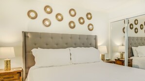 Een net opgemaakt bed met een gestoffeerd hoofdeinde, twee nachtkastjes met lampen, en decoratieve wandkunst.