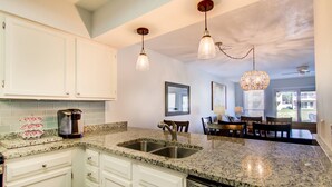 A kitchen with granite countertops, white cabinetry, stainless steel sinks, and pendant lighting.
