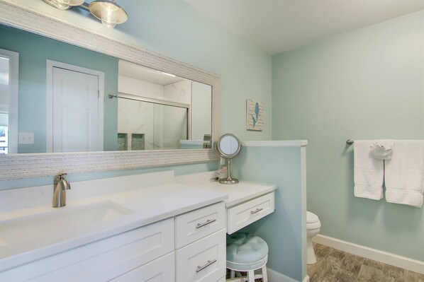A bathroom with a white vanity, a large mirror, a round mirror, and a toilet.