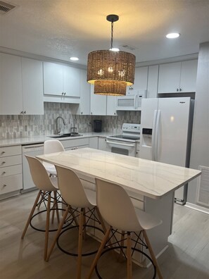 A modern kitchen with white cabinetry, a marble countertop, and a central island with chairs. - 8F, Isle Be Back (Destin)