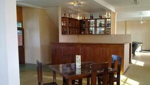 A dining area with a wooden table and chairs, a bar area with shelves of bottles, and a ceiling fan. - Taprospa Tissa (Weerawila)