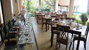 A restaurant with multiple tables and chairs, a buffet line with tea and coffee, and a view of greenery outside. - Taprospa Tissa (Weerawila)