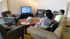 A living room with striped armchairs, a coffee table with a floral centerpiece, and a television displaying a show. - Taprospa Tissa (Weerawila)