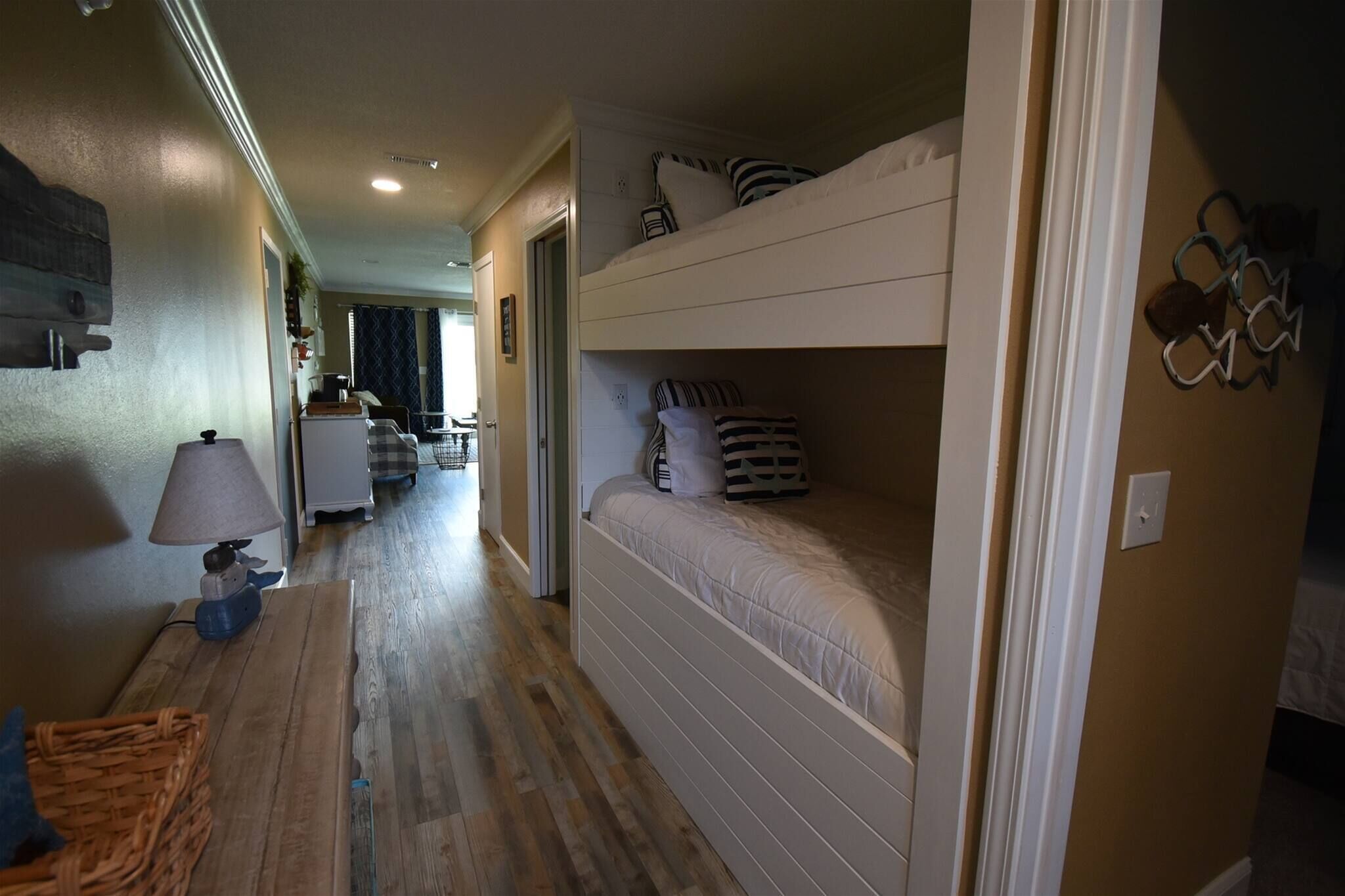 A narrow hallway with a bunk bed on the right, a lamp on the left, and a wooden floor.