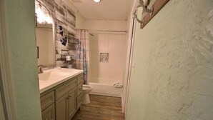 A bathroom with a wooden floor, a white bathtub, a toilet, and a sink with a mirror. - 8B, Beach Please (Destin)