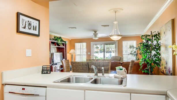 A kitchen with a white countertop, double sink, and built-in dishwasher. There is a dining area with wicker furniture and a ceiling fan. - 4A, Castaway Cove (Destin)