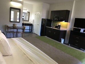 A hotel room with a bed, a small desk with a chair, a kitchenette with a microwave, refrigerator, and a TV. - Studio 6 Chattanooga TN East (Chattanooga)