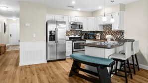 A modern kitchen with white cabinets, stainless steel appliances, and a central island with bar stools. - 7E, Shell We Stay? (Destin)