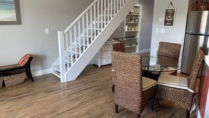 Un coin repas avec des chaises en osier, une table en verre et un escalier blanc.