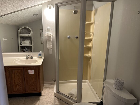 A bathroom with a glass-enclosed shower, a sink with a mirror, and a toilet. - 8E Beachy Keen (Destin)