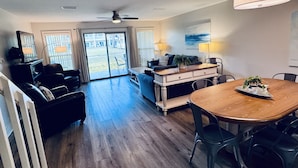 A spacious living area with a wooden floor, a dining table, and a large window with a view of the outdoors.
