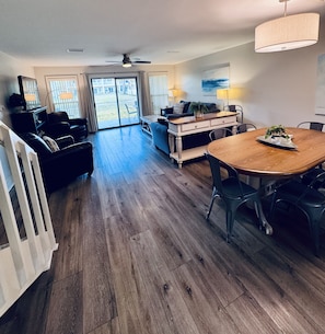 A spacious living area with a wooden floor, a dining table, and a large window with a view of the outdoors.