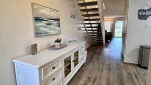 A spacious room with a wooden floor, a white dresser, a painting, and a staircase.