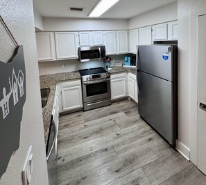 Una cocina con armarios blancos, un refrigerador de acero inoxidable, un microondas y un horno.