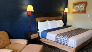A hotel room with a bed, two bedside lamps, a chair, and a small table. - Capt. John Smith Inn (Williamsburg)
