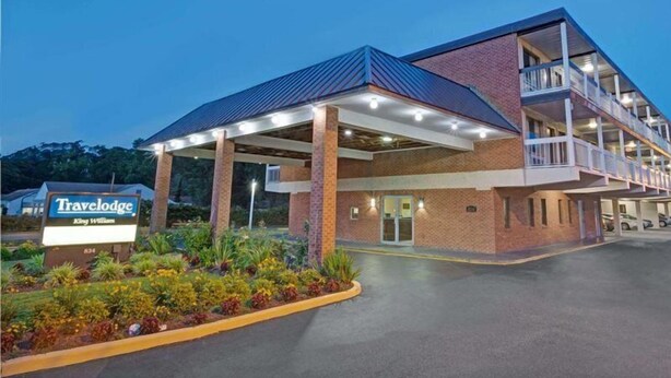 A Travelodge King William with a covered entrance, brick exterior, and a landscaped garden area. - Capt. John Smith Inn (Williamsburg)