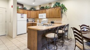 A kitchen with wooden cabinets, a white refrigerator, a microwave, a sink, and a dining area with a table and chairs. - King Bedroom, 1 Bathroom + Adjoining Queen Suite Golf Condo (Branson)