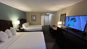 A hotel room with two beds, a desk, a television, and a door.